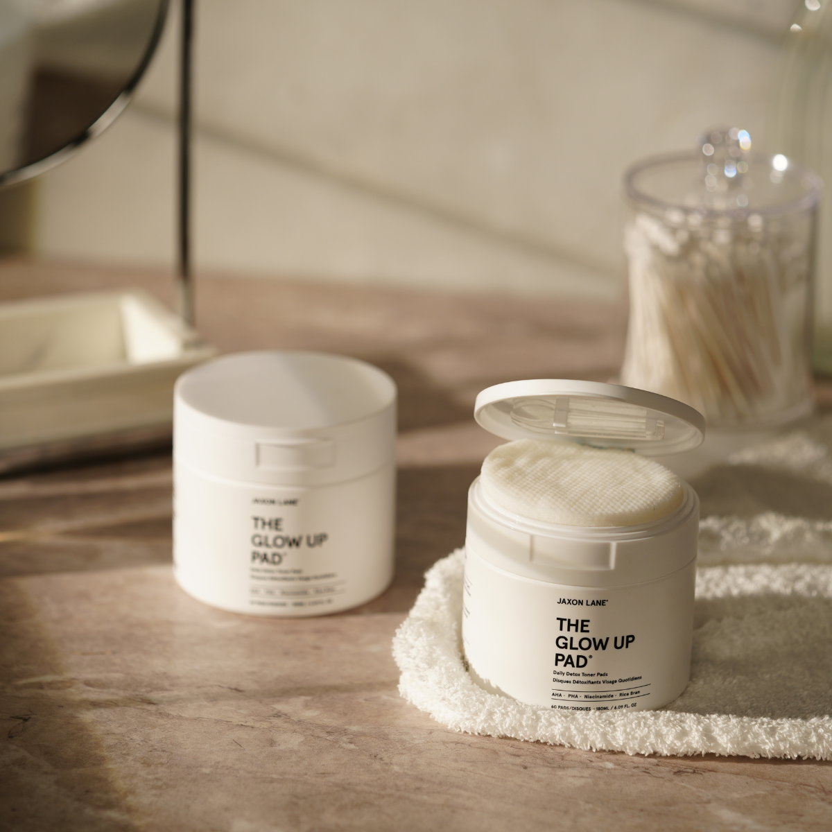 Two jars labeled 'The Glow Up Pad' on a wooden surface with a blurred background.