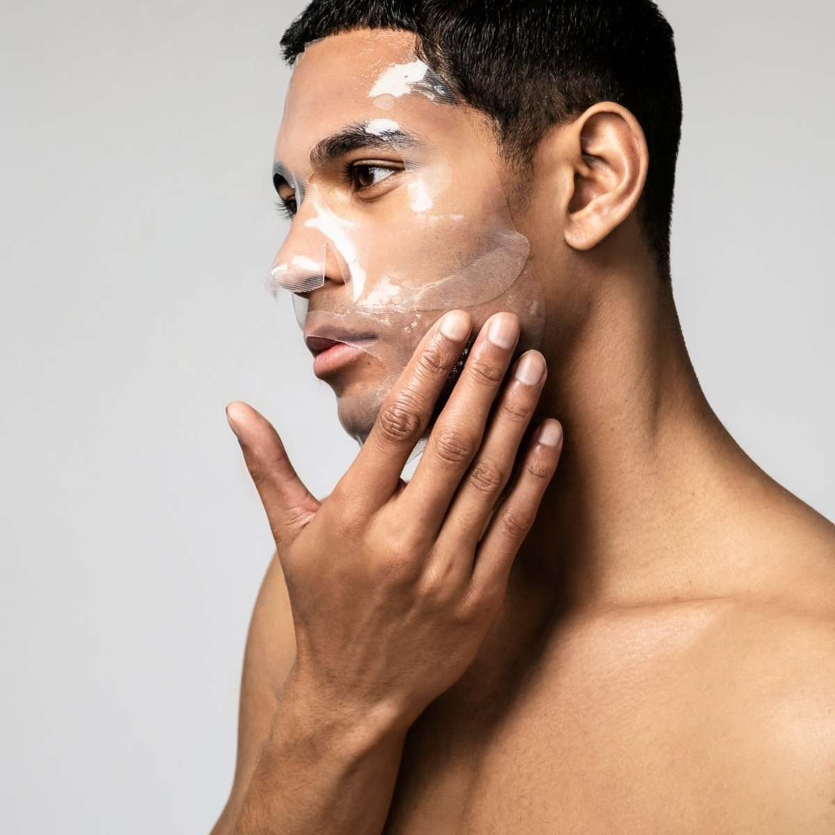 Man applying a facial mask on his face with a neutral background
