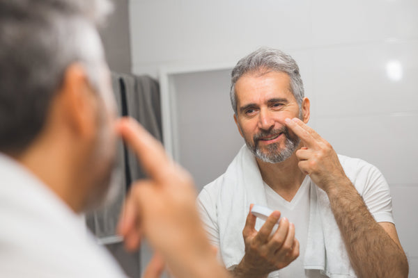 65 year old man applying facial cream while looking in the mirror