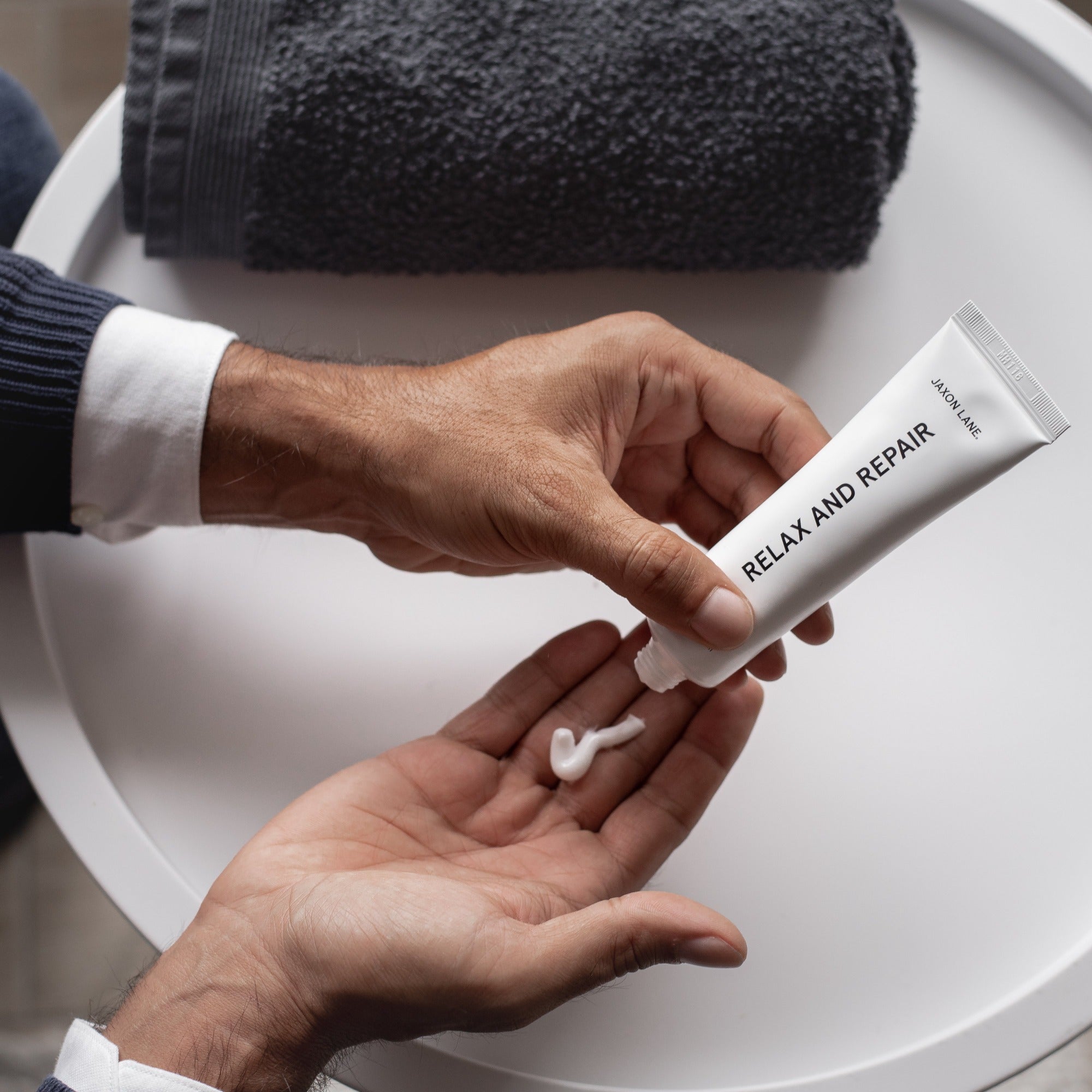 a person squeezing moisturizer out of Jaxon Lane's Relax and Repair product bottle into his hands.