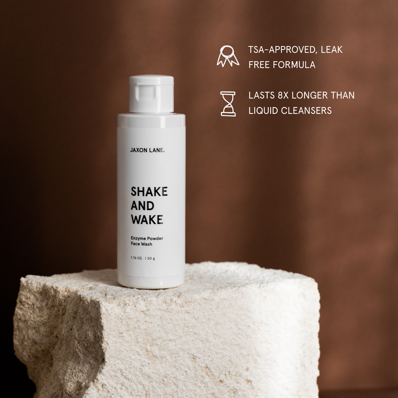 White bottle of Jaxon Lane 'Shake and Wake' Enzyme Powder Face Wash on a textured surface with brown background