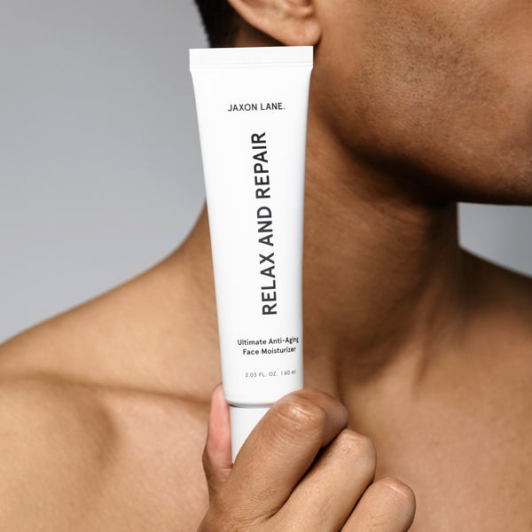 Hand holding a tube of 'Relax and Repair' face moisturizer against a neutral background